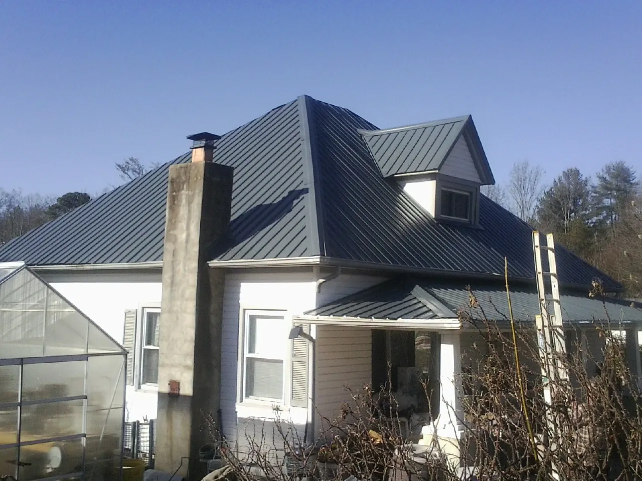 Dark blue standing seam metal roof on a white farmhouse with dormer — Slate & Tile Roof Repair by Roofing Brothers in Eads