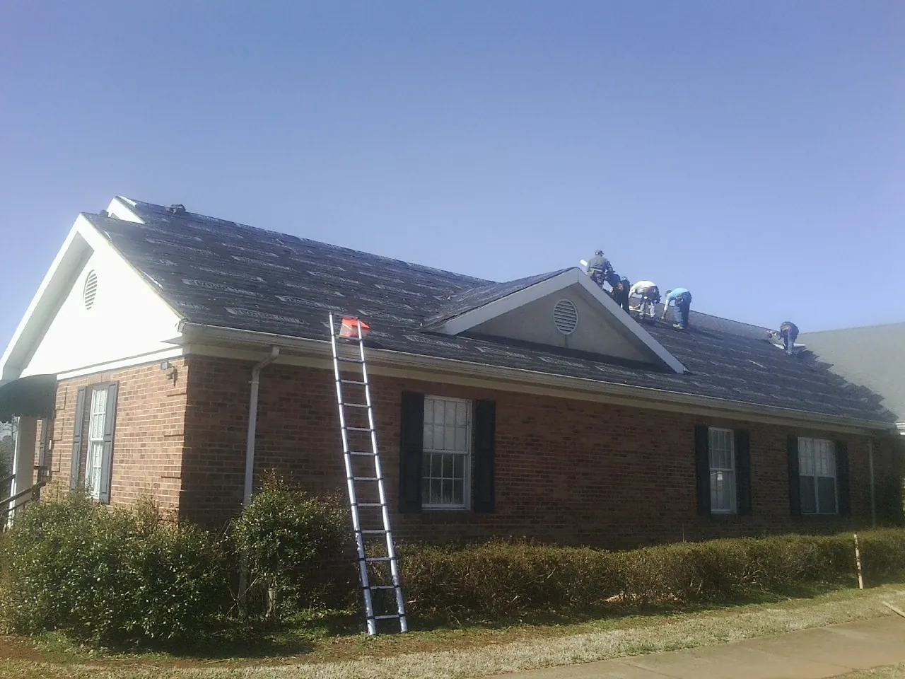 Crew tearing shingles off a brick ranch roof with a ladder set — Emergency Roof Repair work by our crew in Eads