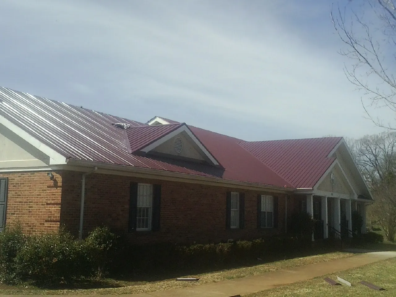 Red metal roof with gabled entries on a long brick building, from a Hail Damage Roof Repair job in Eads