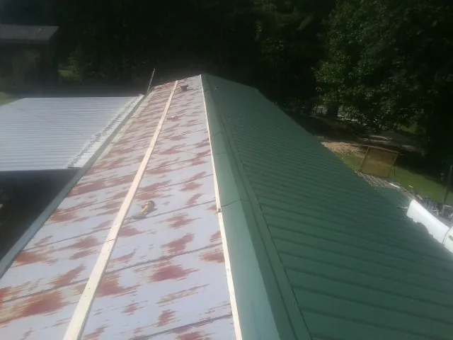 Old rusted panels beside newly installed green metal roofing — Wind Damage Roof Repair by Roofing Brothers in Eads