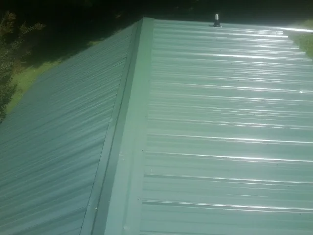 New green metal panels meeting at the ridge of a roof — Flat Roof Repair work by our crew in Eads