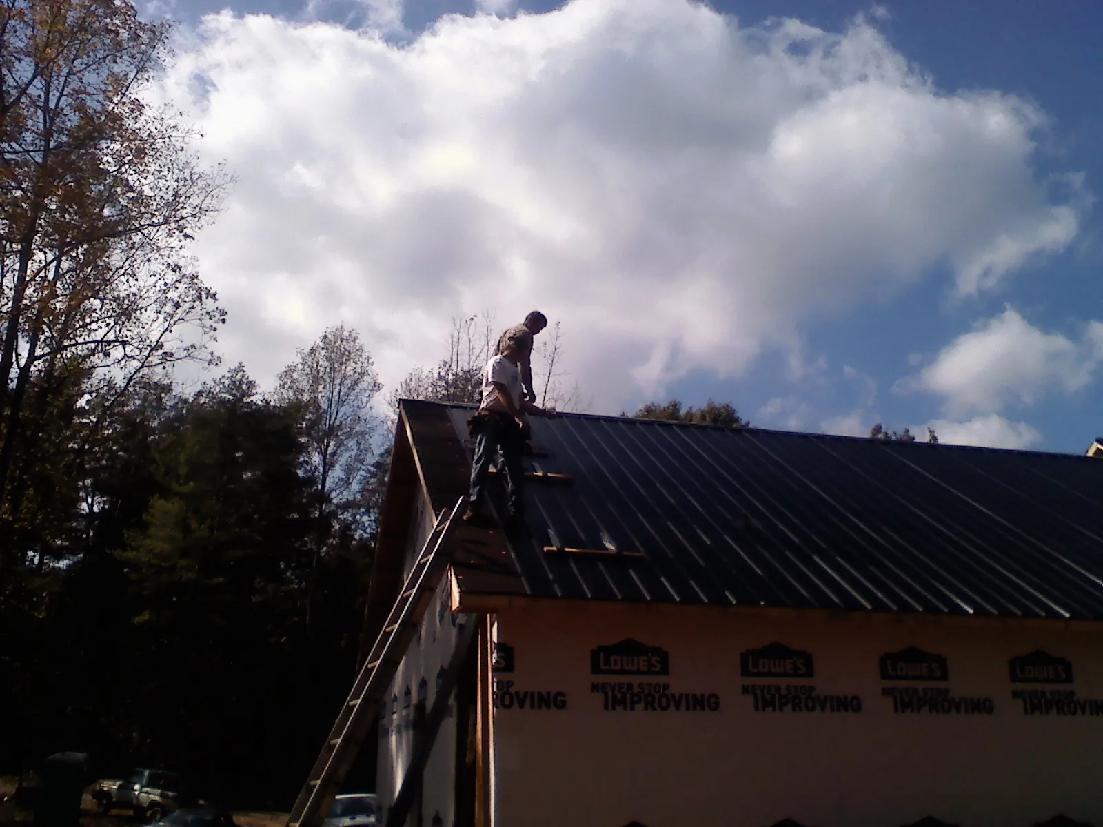 Roofer fastening dark metal panels high against a cloudy sky, from a Roof Inspection job in Eads
