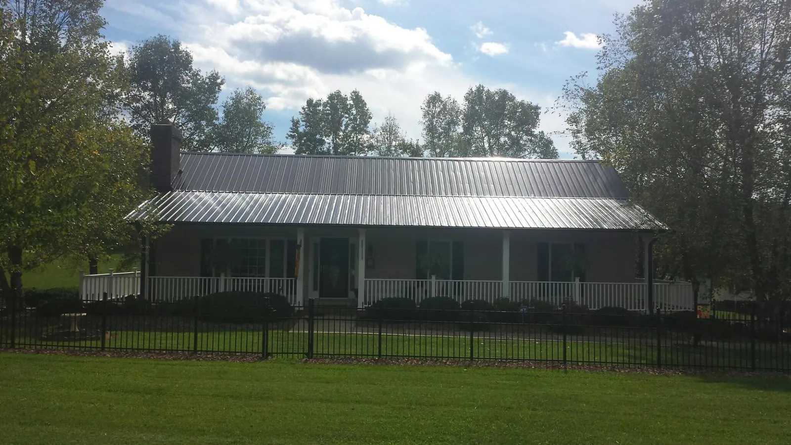 Gray metal roof on a brick ranch with a full width front porch — Gutter Guard Installation work by our crew in Eads