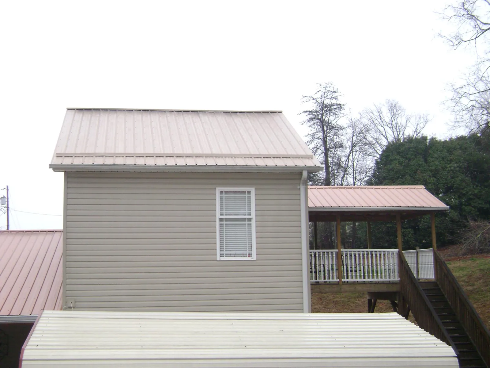 Tan metal roofs on a two story addition and attached porch, from a Roof Replacement job in Eads